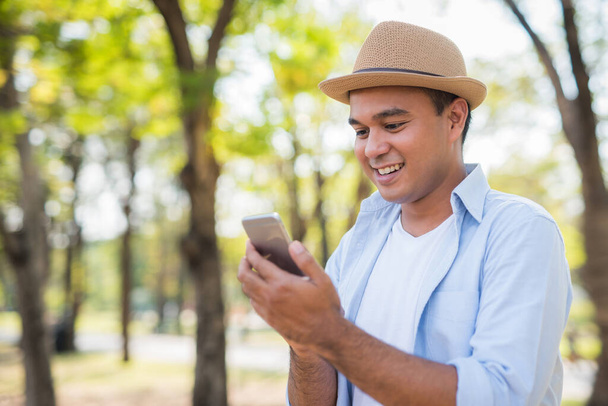 Νεαρός τυχαίος Ασιάτης που χρησιμοποιεί smartphone στο πάρκο - Φωτογραφία, εικόνα