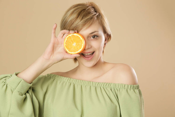 Όμορφη ευτυχισμένη γυναίκα που κρύβεται πίσω από πορτοκαλί φέτα. Έννοια της βιταμίνης C οφέλη για την επιδερμίδα του δέρματος. - Φωτογραφία, εικόνα