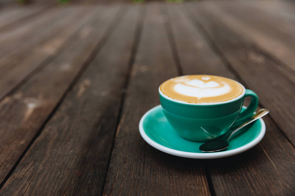 Hot aromatic cappuccino coffee in a turquoise-coloured cup with latte art on wooden table with blur background. Concept of cafe and bar, barista art.  - Photo, Image
