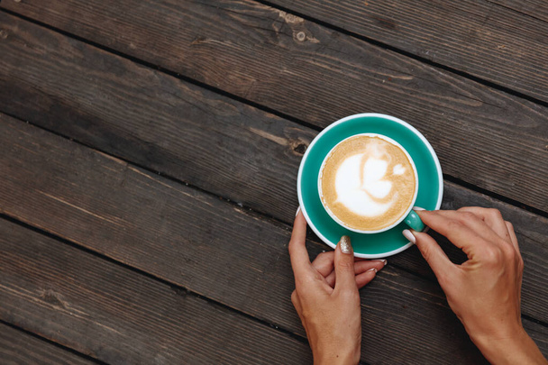 Une tasse de café frais chaud bleu clair avec un magnifique latte art fabriqué par un barista professionnel. Boisson chaude du matin servie sur soucoupe pour jeune femme sur table en bois
. - Photo, image