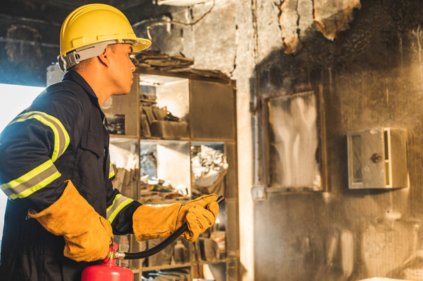 Mladý asijský hasič, hasiči používají hasicí přístroje, které hoří v budově. - Fotografie, Obrázek