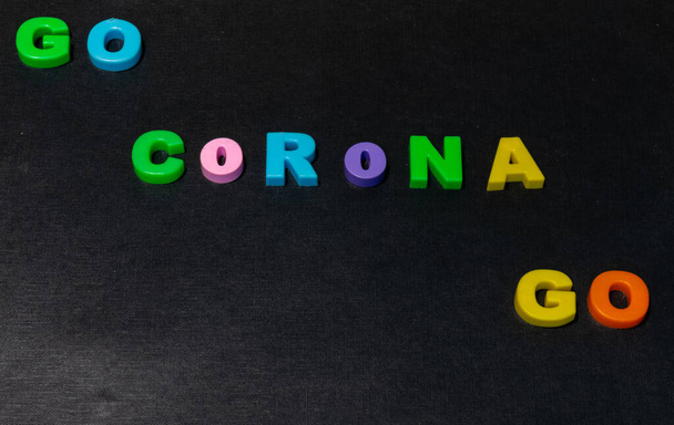 Οι λέξεις GO CORONA GO για vector scrabble αλφάβητο πλακάκια πάνω από ένα μαύρο ξύλινο φόντο. Μείνετε στο σπίτι και να είστε ασφαλείς - Φωτογραφία, εικόνα