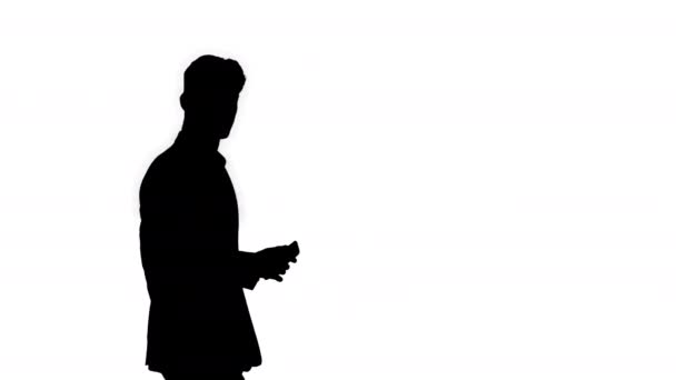 Silhouette Handsome suspicious businessman walking by with a phone in a hand and with briefcase looking to the side. - Πλάνα, βίντεο
