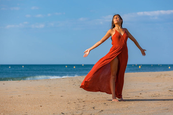 Досить молода жінка в червоній сукні і оголені ноги на піску пляжу. Щаслива дівчина насолоджується свободою на морі
 - Фото, зображення
