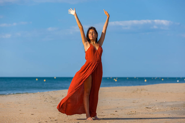 Jolie jeune femme en robe rouge et pieds nus sur le sable de la plage. Fille heureuse jouissant de la liberté à la mer
 - Photo, image