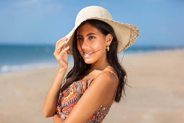 Egy csinos fiatal nő portréja szalmakalapban a parton. Boldog mosolygós lány. - Fotó, kép