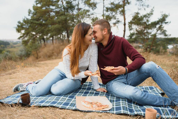 Young couple sitting on park bench and eating pizza.Fast food.Woman and man having picnic at sunset. Guys relaxing and enjoying food. Lifestyle - Foto, imagen