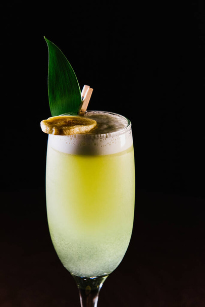 The yellow cocktail is decorated with a banana on a dark background. - Photo, image