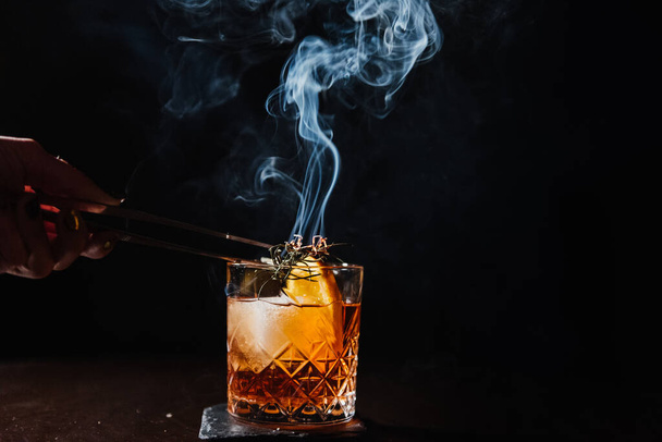 Whiskey with ice, orange and rosemary smoking. - Фото, изображение