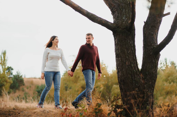 Beautiful young couple walking in autumn park - Фото, изображение