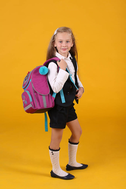 Retrato de una niña de primer grado en uniforme escolar con pelo largo y fluido sobre un fondo amarillo con una mochila
 - Foto, Imagen