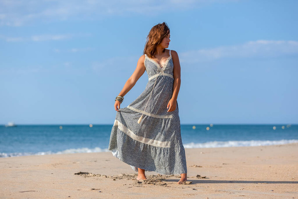 Mooie jonge vrouw in een jurk en naakte voeten op het strand. gelukkig meisje genieten van vrijheid op de zee - Foto, afbeelding