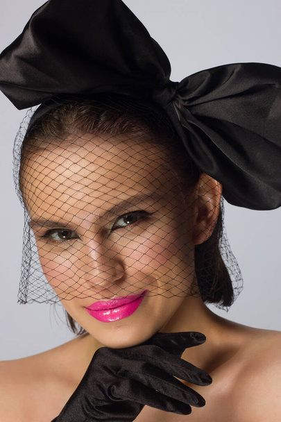 Fashionable half beauty of a woman with a knot and veil, black eyeliner and pink lipstick. Clean and radiant skin, natural lip gloss, thick eyebrows and long eyelashes. Cosmetology and makeup. - Photo, image
