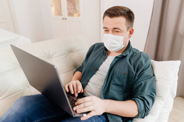 man blogger in medical mask working lying on couch - Fotó, kép