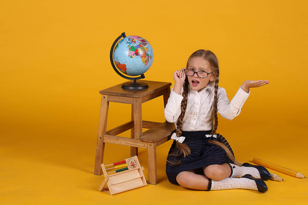 Caucasian first grader with long braids on a yellow background with a globe with the image of Africa, Europe, America - Fotografie, Obrázek