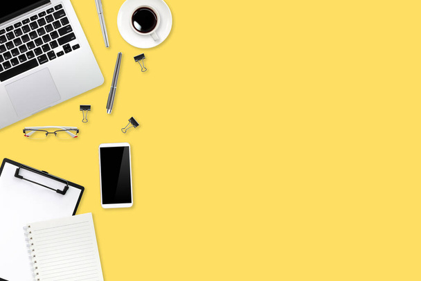 digitaler Marketing-Schreibtisch mit Laptop, Bürobedarf, Kaffeetasse und Handy auf gelbem Pastell-Hintergrund - Foto, Bild