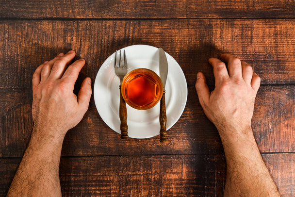 Ένας άνθρωπος αντιμετωπίζει τον εθισμό στο αλκοόλ, κονιάκ σε ένα πιάτο με ένα πιρούνι και μαχαίρι. - Φωτογραφία, εικόνα