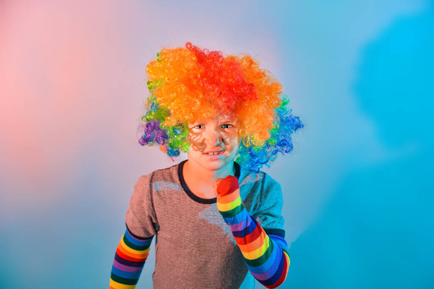 Θυμωμένο και δυσαρεστημένο αγόρι με περούκα κλόουν και πολύχρωμα μανίκια.. - Φωτογραφία, εικόνα