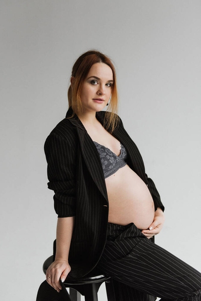 Young pregnant woman in a black suit in the studio on a white background. - Photo, Image
