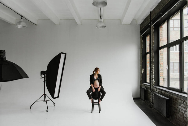 Νεαρή έγκυος γυναίκα με μαύρο κοστούμι στο στούντιο σε λευκό φόντο. - Φωτογραφία, εικόνα