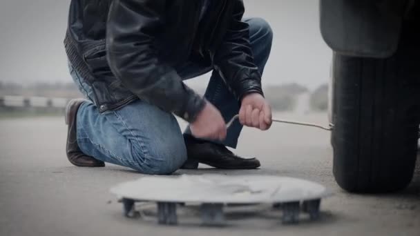 um homem com um macaco abaixa o carro para substituir as rodas em uma estrada deserta
 - Filmagem, Vídeo
