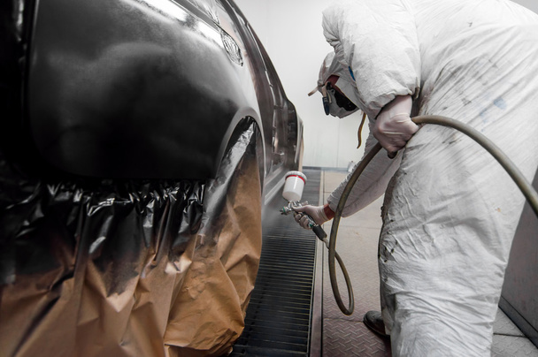 Trabajador automático rociando pintura negra en un coche en un garaje de automóviles con equipo de protección
 - Foto, Imagen