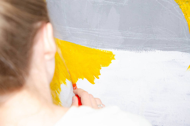Νεαρό κορίτσι σχεδιαστής σχεδιάζει μια πόλη σχέδιο με χρώματα σε ένα γκρίζο τοίχο - Φωτογραφία, εικόνα