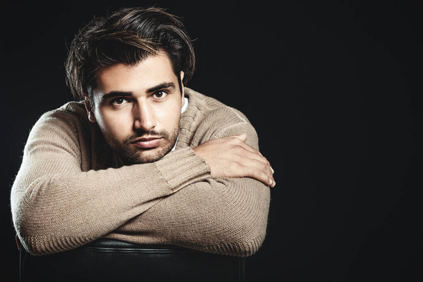 Pensive young man with folded arms. Looking at the camera. Trendy hair, brown sweater and dark background. - Foto, afbeelding