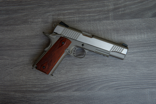 Nerezová ruční pistole s hnědou rukojetí je na dřevěné podlaze - zahájena - Fotografie, Obrázek