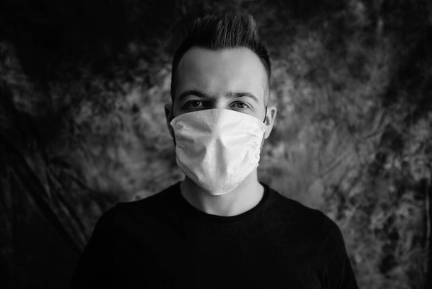 Sick young man with medical face mask portrait close up illustrates pandemic coronavirus disease on dark background. Covid-19 outbreak contamination concept. - 写真・画像
