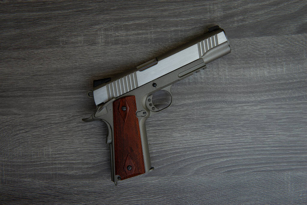 Бесшумный пистолет с коричневой рукояткой лежит на деревянном полу
  - Фото, изображение