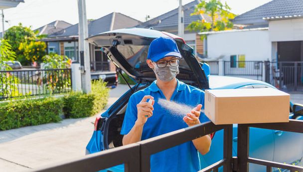 Asian Young delivery man courier online with box in uniform he protective face mask and squirt spray sanitizing, service customer front of house under curfew quarantine pandemic coronavirus COVID-19 - Photo, image