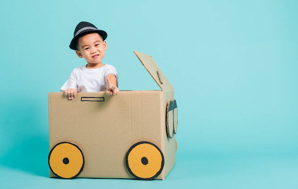 Happy Asian children boy smile in driving play car creative by a cardboard box imagination, summer holiday travel concept, studio shot on blue background with copy space for text - Photo, Image