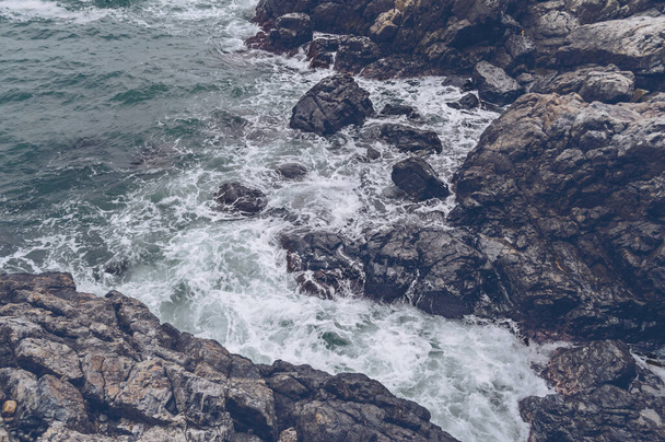 view form above on rolling waves of rugged stone shore on gloomy day - Фото, изображение
