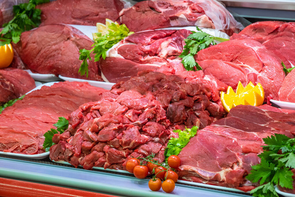 Fleischabteilung in einer Metzgerei in einem Einkaufszentrum. Verschiedene Fleischsorten werden auf geordnete und kreative Weise präsentiert. Regale eines Lebensmittelmarktes. Orangen und Gemüse als Dekoration und Belag. - Foto, Bild