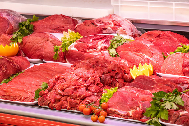 Bir alışveriş merkezinde kasaplık yapan et bölümü. Düzenli ve yaratıcı bir şekilde gösterilen çeşitli et türleri. Yiyecek süpermarketinin rafları. Süsleme ve süsleme için portakal ve sebze. - Fotoğraf, Görsel