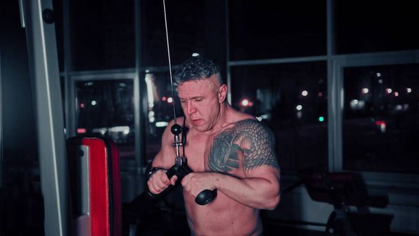 Homem duro com tatuagem no ombro treinando suas mãos no ginásio usando simulador de treinamento de mão
 - Foto, Imagem
