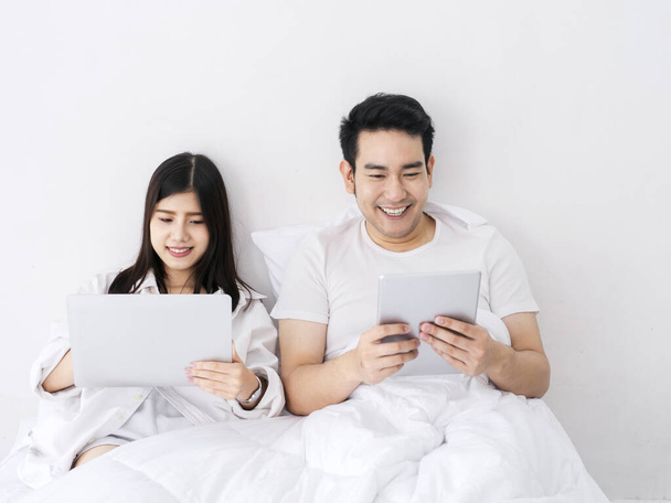 Щаслива азіатська пара, що використовує планшет і ноутбук на ліжку, працює з дому, залишається вдома, зберігайте безпечну концепцію. - Фото, зображення
