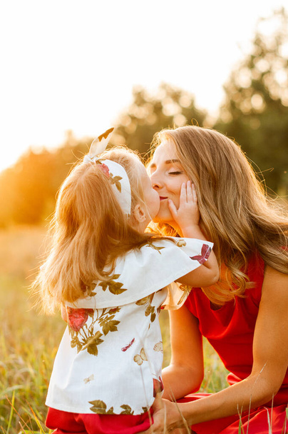 A kislány megcsókolja anyát a mezőn napsütésben. - Fotó, kép
