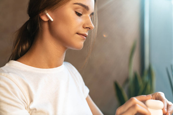 Photo of caucasian young woman in basic t-shirt using earpods while sitting in cozy cafe - Valokuva, kuva