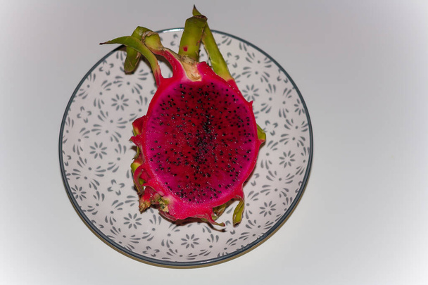 Frische exotische halbierte Pitaya oder Pitahaya costaricensis, Drachenfrucht auf Teller auf weißem Hintergrund. - Foto, Bild