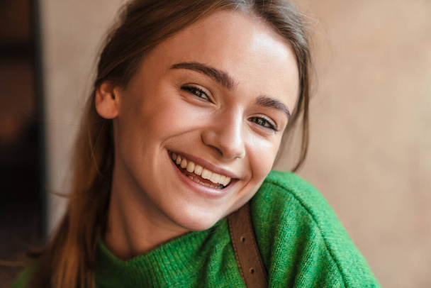 Foto de la hermosa mujer feliz en suéter verde mirando y riéndose de la cámara en el acogedor café
 - Foto, Imagen