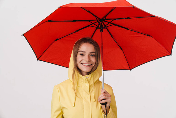Photo of joyful beautiful woman in raincoat holding umbrella and smiling isolated over white background - Zdjęcie, obraz