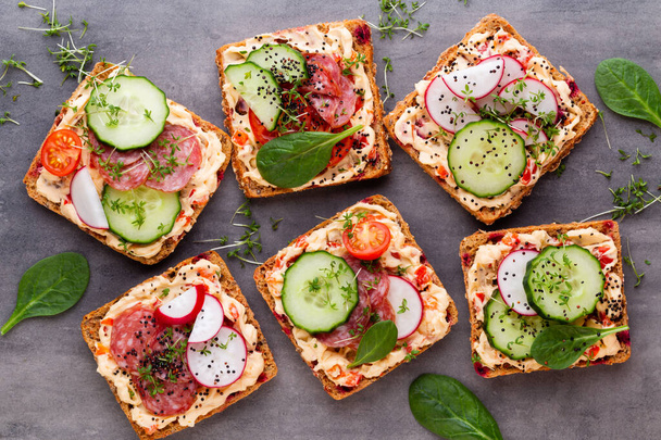 Sandwiches with cream cheese, vegetables and salami. Sandwiches with cucumber, radish, tomatoes, salami on a gray background, top view. Flat lay. - Fotó, kép