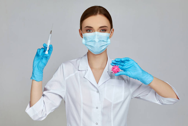 woman doctor in mask and rubber gloves holding syringe and virus model - Фото, изображение