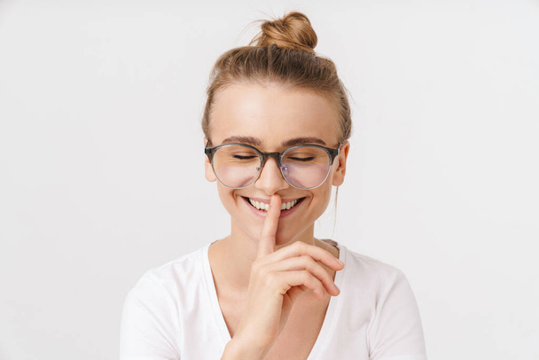Photo of cheerful caucasian woman in eyeglasses making silence gesture isolated over white background - 写真・画像