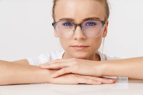 Photo of beautiful serious woman in eyeglasses looking at camera while leaning on table isolated over white background - Φωτογραφία, εικόνα
