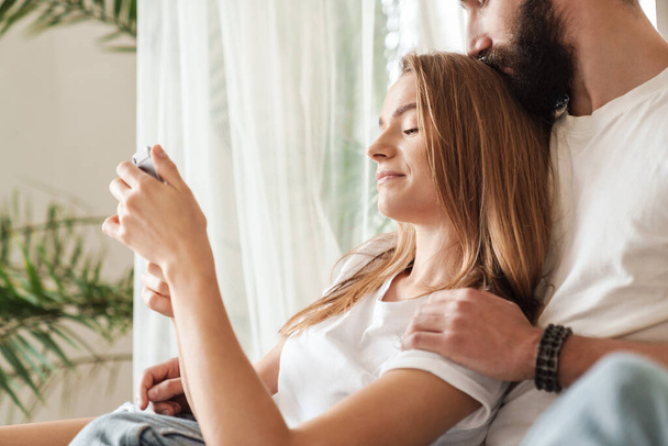 Pretty young couple lying on sofa at home and using smartphone - Foto, imagen