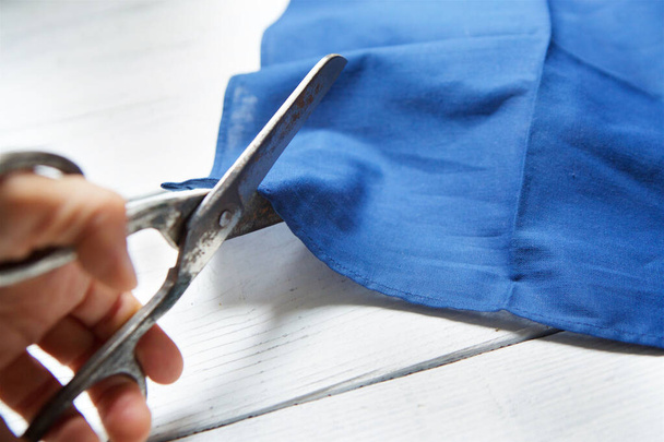 Tijeras herramienta en la mano de un hombre cortar la tela de color azul. El concepto de hobby y creatividad
. - Foto, Imagen