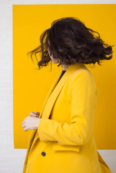 Stylish young woman in a yellow jacket on a yellow background, happy and dancing. - Fotografie, Obrázek